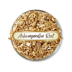May include: A clear glass bowl filled with chopped ashwagandha root. The root pieces are light brown and beige. A gold-edged label with the words "Ashwagandha Root" is placed over the root.