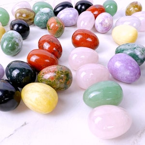Puede incluir: Una colecci&oacute;n de huevos de piedras preciosas pulidas en varios colores, incluyendo verde, rosa, rojo, amarillo, morado y negro. Los huevos est&aacute;n dispuestos sobre una superficie de m&aacute;rmol blanco.
