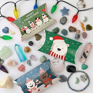 May include: Three small pillow boxes with festive Christmas designs. The boxes feature penguins, a polar bear, and a bear wearing a scarf. The boxes are surrounded by various crystals, stones, and other decorative items.