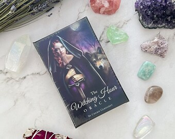May include: A deck of oracle cards with a dark purple background and a woman in a black hooded cloak holding a sword. The text on the box reads "The Witching Hour Oracle by Cherie Gerhardt".