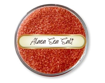 May include: A clear glass jar filled with coarse, reddish-orange Alaea Sea Salt. The jar has a gold-bordered label with the words "Alaea Sea Salt" in elegant script. The salt crystals fill the jar, creating a textured, granular appearance.