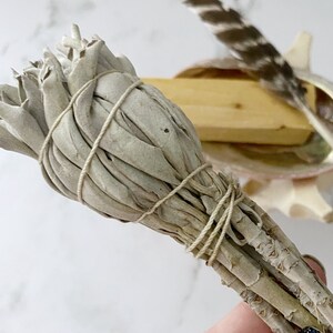 Puede incluir: Un manojo de salvia blanca atado con cuerda, listo para usarse en un ritual de limpieza.