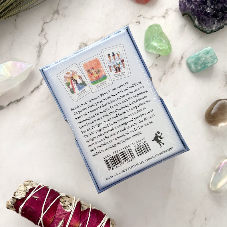 May include: A Simplicity Tarot deck box, featuring Rider-Waite artwork, with three tarot cards visible. The box has text describing the deck's features, including keywords on the card faces and a 100-page guidebook. The deck includes 80 cards.