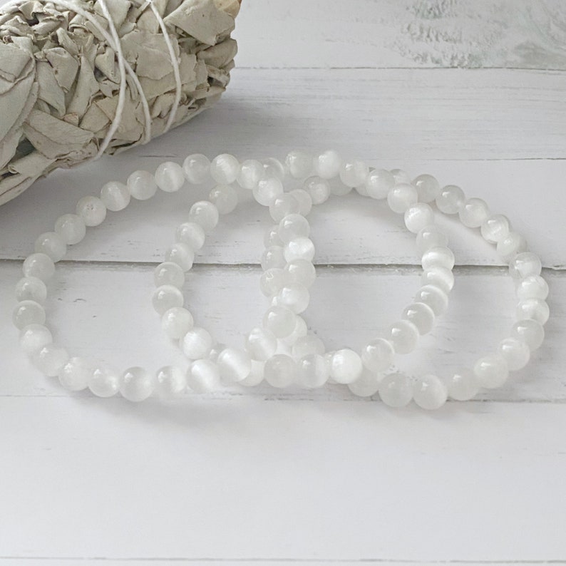 Peut inclure: Trois bracelets en pierres blanches empil&eacute;s sur une surface en bois blanc. Les bracelets sont faits de perles rondes et lisses.
