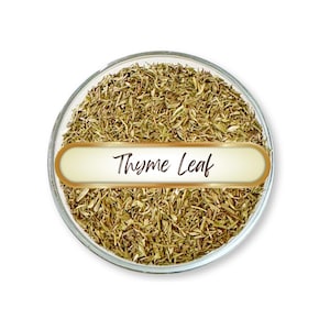 May include: A clear glass bowl filled with dried thyme leaves. A gold-bordered label across the bowl reads "Thyme Leaf" in a cursive font. The thyme is a light brown color.