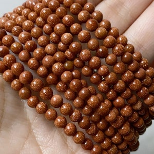May include: A strand of brown, round, gemstone beads with a speckled texture. The beads are strung together on a clear thread.
