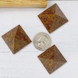 May include: Three brown and yellow patterned stone pyramids with a quarter coin in the center. The pyramids are square-based and have a textured surface. A piece of wood is in the background.