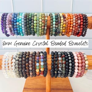 May include: A display of beaded bracelets in various colors, including purple, blue, green, orange, and red. The bracelets are 8mm in size and made of genuine crystal. The text on the image reads "8mm Genuine Crystal Beaded Bracelets".