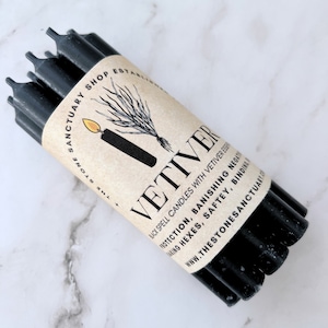 May include: A bundle of black spell candles wrapped in a tan paper label. The label features the word "VETIVER" in large letters, along with text about protection and banishing negativity. The Stone Sanctuary Shop is also printed on the label.