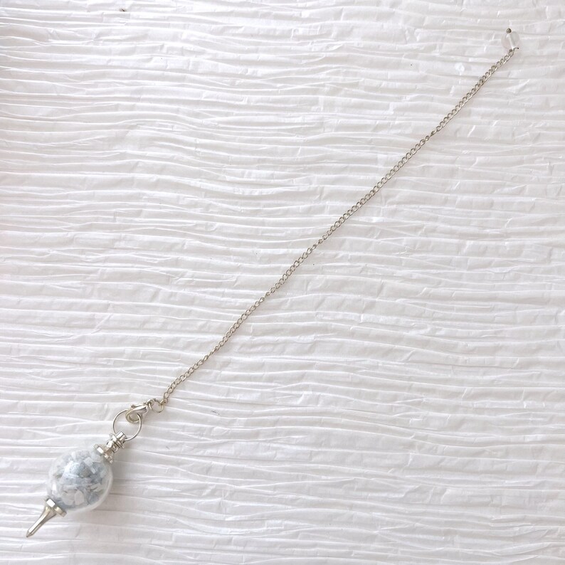May include: A silver chain with a white and gray stone pendulum. The pendulum is round and has a pointed tip.