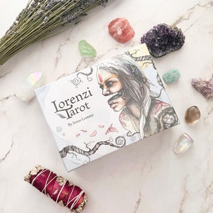 May include: A white box with the text "Lorenzi Tarot" and "By Irene Lorenzi" on the front. The box features a colorful illustration of a woman with a headdress and a lion.