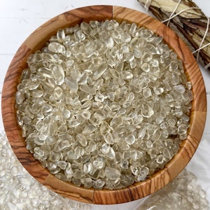 Puede incluir: Un cuenco de madera lleno de trozos de cuarzo transparente. El cuenco est&aacute; hecho de madera marr&oacute;n claro y tiene un patr&oacute;n de veta natural. Los trozos de cuarzo son peque&ntilde;os y transl&uacute;cidos, con un ligero tono amarillo.