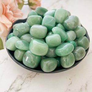 May include: A bowl filled with smooth, green tumbled stones. The stones are a light green color and have a polished finish.