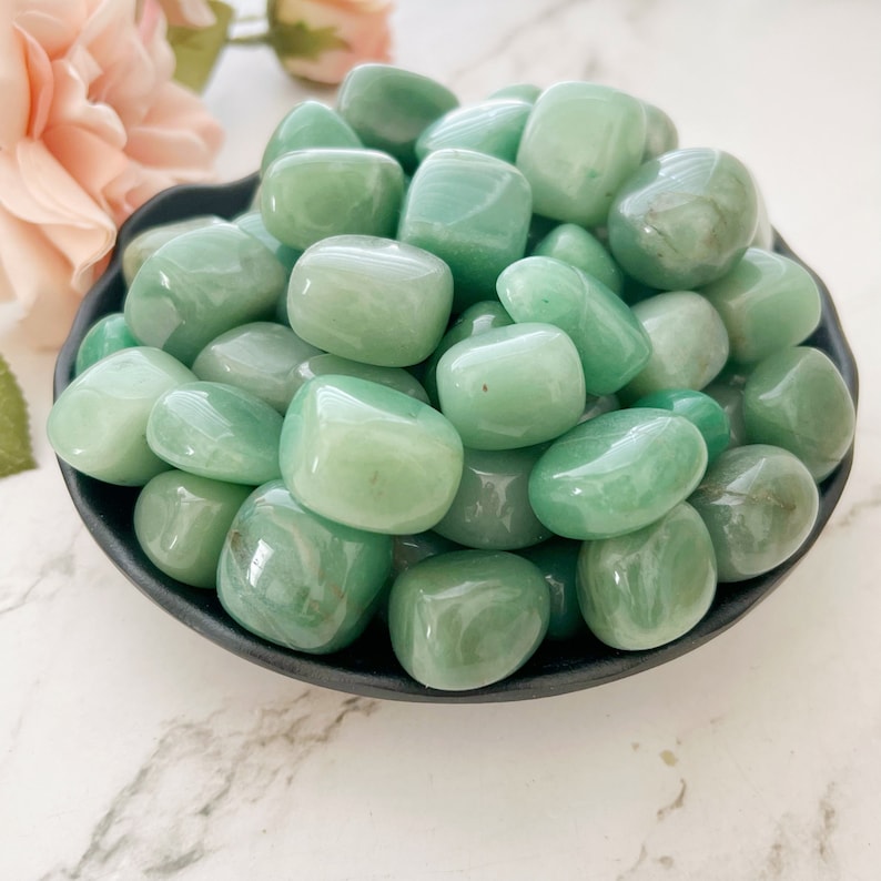 May include: A bowl filled with smooth, green tumbled stones. The stones are a light green color and have a polished finish.