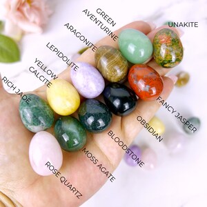 Puede incluir: Una colecci&oacute;n de 12 huevos de piedras preciosas pulidas, cada uno con un color y un patr&oacute;n diferentes. Los huevos est&aacute;n etiquetados con los nombres de sus piedras preciosas correspondientes, incluyendo aventurina, verde, aragonito, unakita, jaspe fantas&iacute;a, obsidiana, lepidolita, calcita amarilla, jade rico, &aacute;gata musgosa, piedra de sangre y cuarzo rosa.