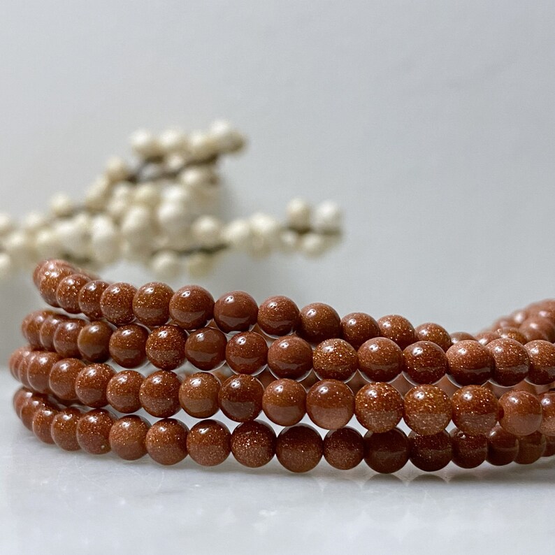 May include: A strand of brown sandstone beads, with a speckled texture, arranged in a circular pattern.