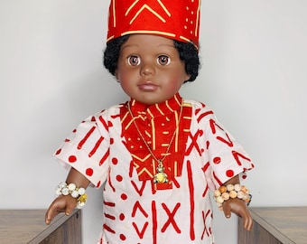 Puede incluir: Una muñeca roja y blanca que lleva un sombrero rojo con un patrón geométrico amarillo, una camisa blanca con patrones geométricos rojos y amarillos, pantalones rojos con un patrón geométrico amarillo y zapatos negros. La muñeca tiene ojos marrones y cabello negro.