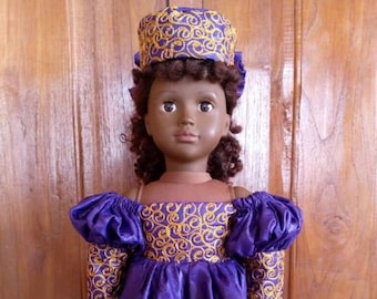 Puede incluir: Un vestido morado con bordados dorados y un sombrero morado a juego con ribetes dorados. El vestido tiene mangas abullonadas y una falda completa. La muñeca lleva zapatos negros.