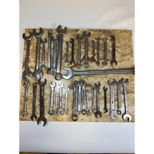 May include: A collection of various silver-toned metal wrenches of different sizes and types, including open-ended and combination styles, arranged in a scattered layout. The tools feature visible markings and show signs of wear and use.