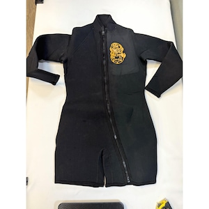 May include: A black wetsuit featuring a long front zipper that extends diagonally toward the left leg. The chest area displays a yellow graphic of a vintage deep-sea diving helmet. The suit has long sleeves and short leg openings.