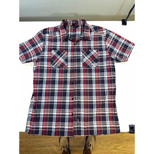 May include: A short-sleeve button-down shirt featuring a plaid pattern in navy blue, white, and red. The shirt includes a standard collar, a full-length front button placket, and two chest pockets with button closures. A small white logo is visible.