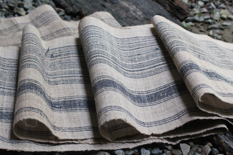 May include: A close-up of a piece of fabric with a striped pattern. The fabric is a light beige color with dark blue stripes. The fabric is folded and wrinkled.