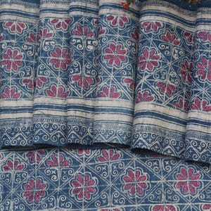 May include: Close-up of a blue and white fabric with a repeating pattern of pink flowers and swirls. The fabric is folded in several places, showing the pattern from different angles.
