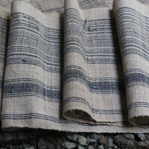 May include: A close-up of a stack of fabric with a striped pattern. The fabric is a light beige color with dark blue stripes. The fabric is folded and layered, creating a textured look.