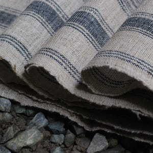 May include: Close-up of a folded piece of fabric with blue and white stripes. The fabric is woven and has a rough texture. The fabric is folded in a way that shows the different layers.