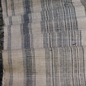 May include: A close-up of a woven fabric with a striped pattern. The fabric is beige with black stripes. The fabric is folded in a way that creates a layered effect.