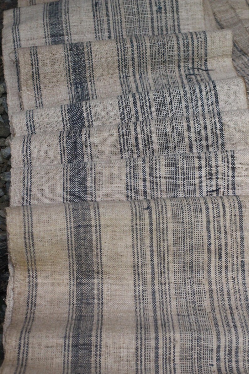 May include: A close-up of a woven fabric with a striped pattern. The fabric is beige with black stripes. The fabric is folded in a way that creates a layered effect.