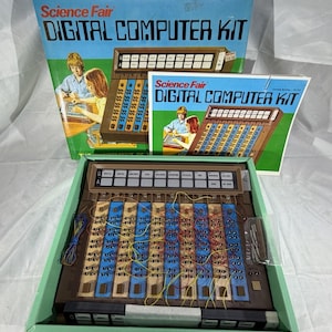 May include: A Science Fair Digital Computer Kit featuring a brown console with blue panels, a white control board, and yellow and red patch wires. The set includes the original box and instruction manual, both displaying the product name and a graphic illustration.