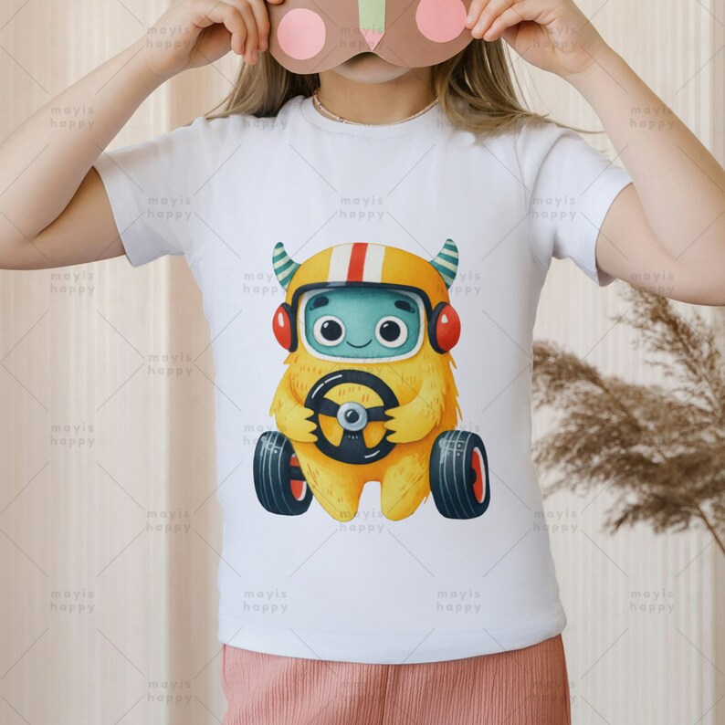 May include: White t-shirt with a cartoon illustration of a yellow monster wearing a helmet and driving a car. The monster has blue eyes and a friendly expression.