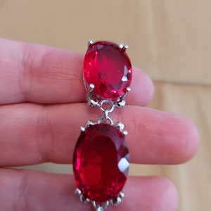 Puede incluir: Un collar de cadena de plata con tres piedras preciosas rojas grandes de forma ovalada. Las piedras preciosas est&aacute;n engastadas en plata.