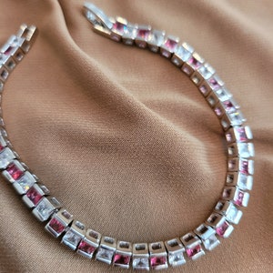 May include: A silver bracelet with alternating pink and clear square-shaped stones.