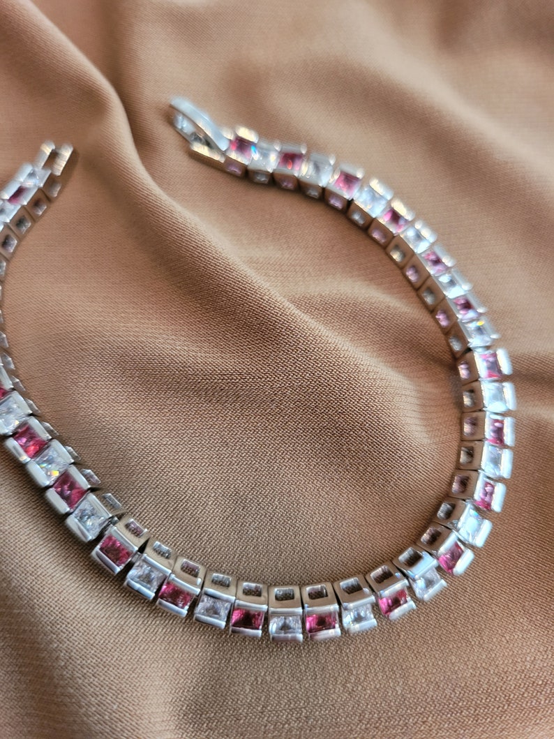 May include: A silver bracelet with alternating pink and clear square-shaped stones.