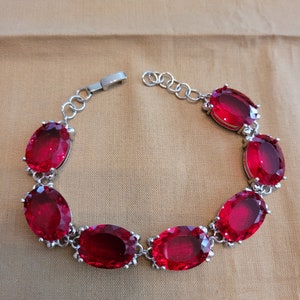 Puede incluir: Un brazalete de plata con una cadena y siete piedras preciosas rojas de forma ovalada.