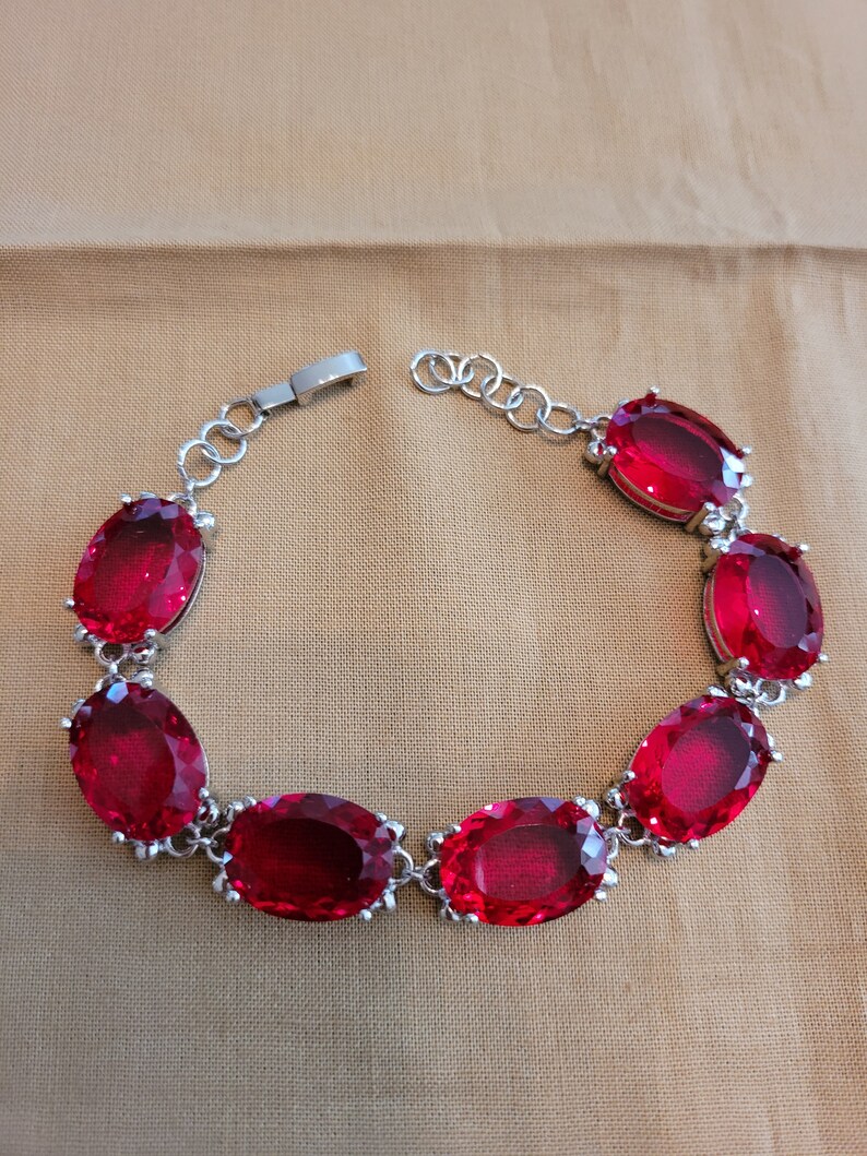 Puede incluir: Un brazalete de plata con una cadena y siete piedras preciosas rojas de forma ovalada.