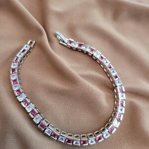 May include: A silver bracelet with alternating pink and white square-shaped stones.