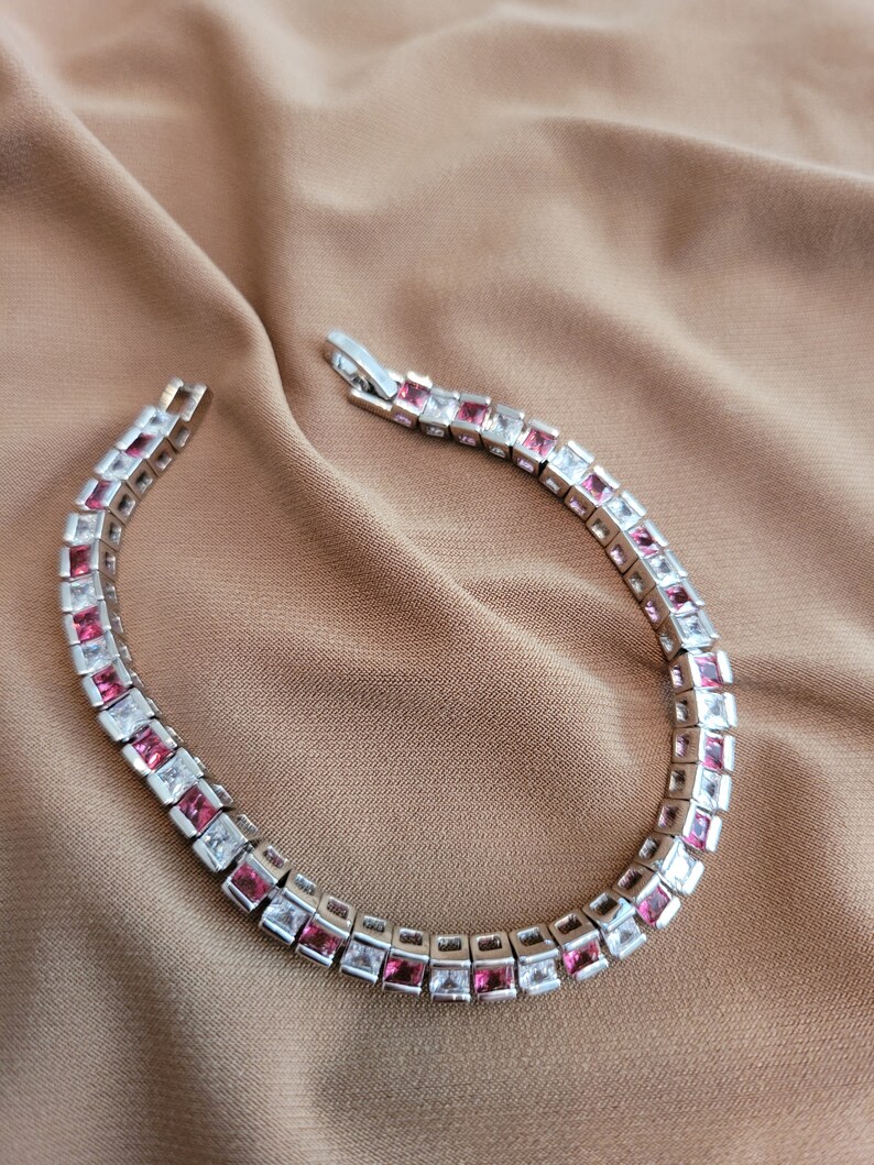 May include: A silver bracelet with alternating pink and white square-shaped stones.