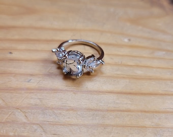 Può includere: Un anello d'argento con una pietra ovale trasparente e tre pietre trasparenti più piccole sulla fascia.