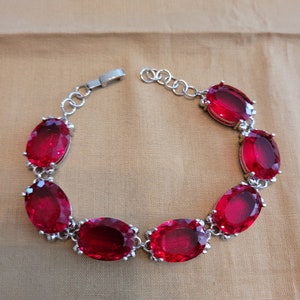 Puede incluir: Un brazalete de plata con un dise&ntilde;o de cadena y piedras preciosas rojas de forma ovalada.