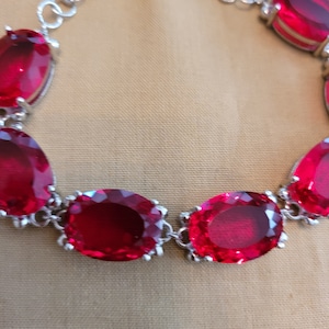 Puede incluir: Un brazalete de plata con piedras preciosas ovaladas rojas. El brazalete tiene un cierre de broche.