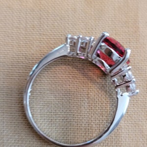 May include: A silver ring with a large red gemstone and smaller clear gemstones on the band.
