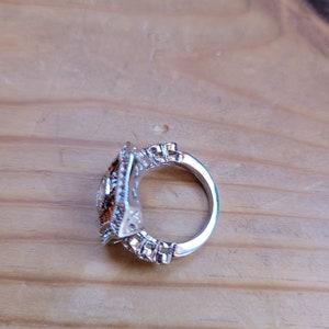 May include: A silver ring with a square-shaped setting featuring a cluster of small, clear and brown stones.
