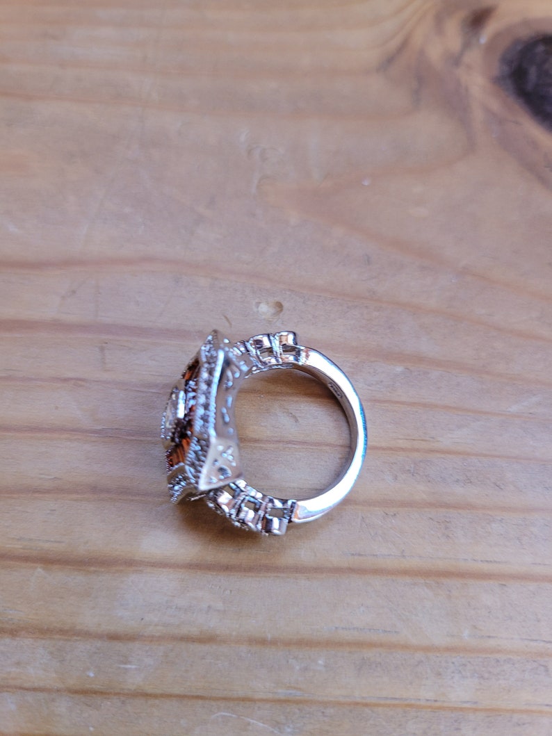 May include: A silver ring with a square-shaped setting featuring a cluster of small, clear and brown stones.