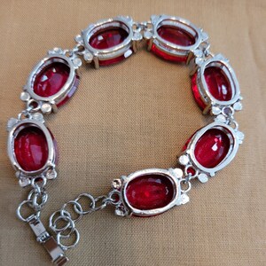 Puede incluir: Un brazalete de plata con cierre de cadena y siete piedras preciosas rojas de forma ovalada.