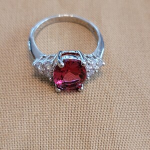 May include: A silver ring with a large, oval-shaped, pink gemstone surrounded by smaller, clear gemstones.