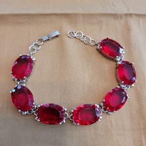 Puede incluir: Un brazalete de plata con un dise&ntilde;o de cadena y seis grandes piedras preciosas ovaladas rojas.