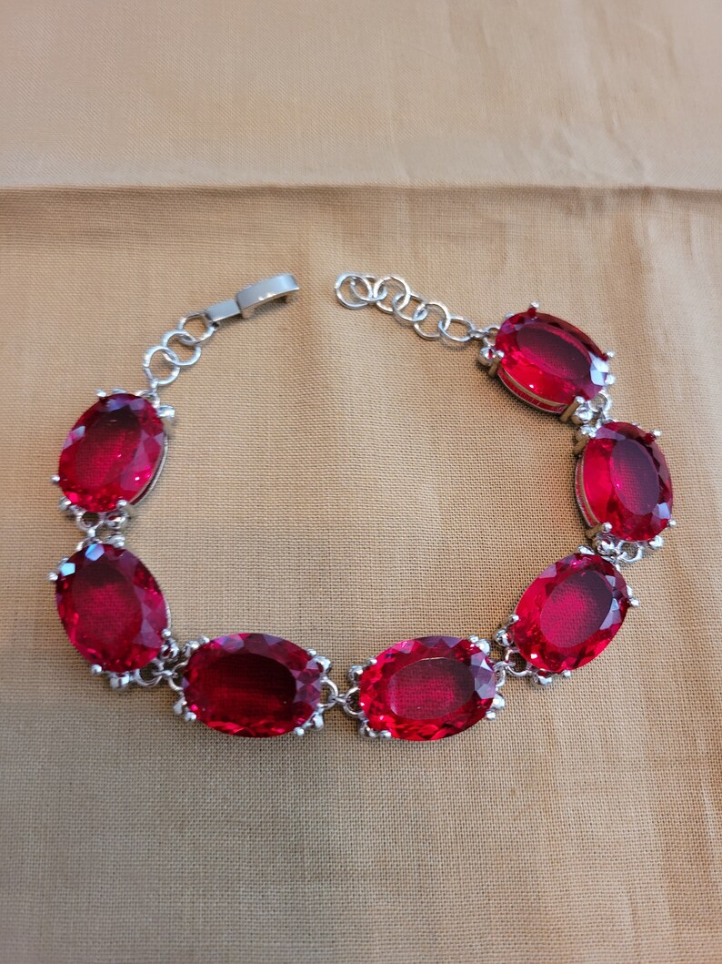 Puede incluir: Un brazalete de plata con un dise&ntilde;o de cadena y seis grandes piedras preciosas ovaladas rojas.